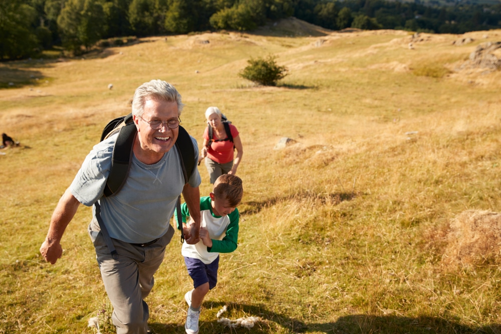 Grandparents,With,Grandchildren,Climbing,Hill,On,Hike,Through,Countryside,In