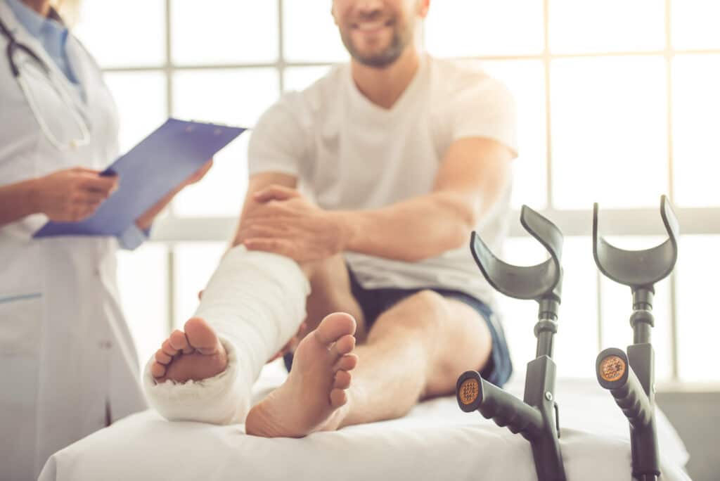 Cropped image of female medical doctor listening to patient with broken leg and making notes while working in her office